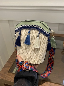 Detail of woven straw bucket bag with blue fringe tassels and geometric patterned strap
