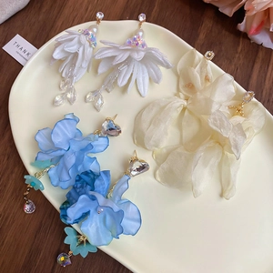 Close-up of floral chiffon earrings in white, beige, and blue with rhinestone details