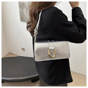 Detail of silver crocodile pattern shoulder bag featuring a gold U-shaped buckle and knotted strap