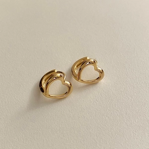 Détail macro de boucles d'oreilles créoles cœur dorées sur une surface crème mate