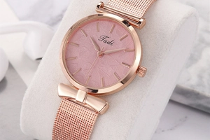 Détail d'une montre en maille or rose avec cadran rose et nœud décoratif élégant