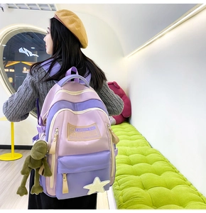 Side view of purple contrast nylon backpack featuring star and frog charms on a model