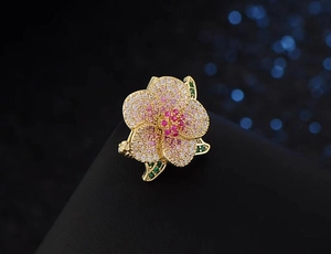 Detailed close-up of camellia brooch with pink and red crystals on golden metal