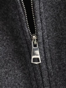 Macro shot of silver metal zipper detail on a dark grey wool coat with fabric texture