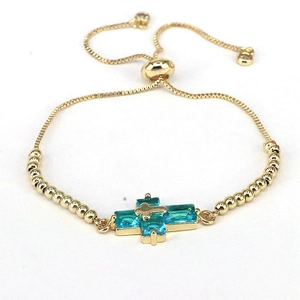Detail of adjustable gold bead bracelet with blue crystal cross pendant on white background