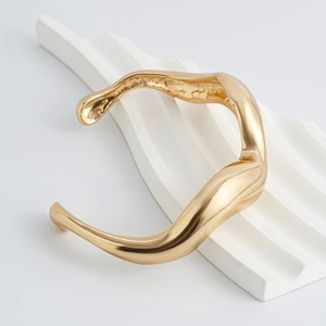 Men's minimalist gold wavy irregular open cuff bracelet on white pedestal display