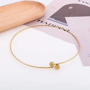 Minimalist gold metal collar necklace with spherical bead ends on a wooden tray