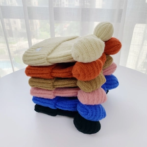 Stacked collection of colorful knit beanies with fluffy pom poms and side woven labels