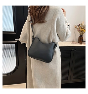 Fashionable black crescent shoulder bag shown on model in an elegant interior setting