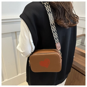 Brown leather crossbody bag detail with red heart print and geometric strap