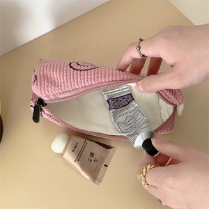 Pink corduroy makeup bag detail showing hand placing cream in the spacious interior