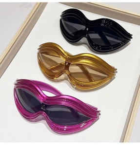 Three Y2K wavy shaped sunglasses in black, amber and pink on white display tray