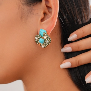 Detailed view of turquoise acrylic stud earrings with crystals and green enamel on a model