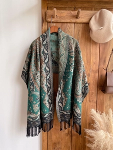 Detail of vintage green paisley shawl with brown patterns and tassel fringe on a wooden hanger