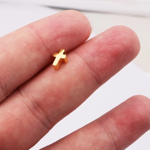 Petit pendentif croix en acier doré poli tenu entre les doigts pour montrer la taille