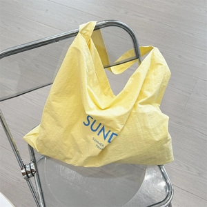 Detail of a bright yellow tote bag with blue typography hanging on a modern chair