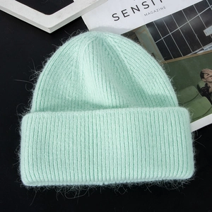 Detailed texture of mint green long rabbit fur knit winter hat on a dark surface