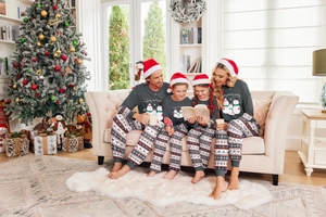 Family of four wearing matching Christmas pajamas sitting on a sofa in a festive home setting