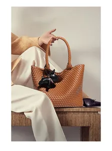 Detail of caramel woven leather tote bag featuring a cute black bulldog charm accessory