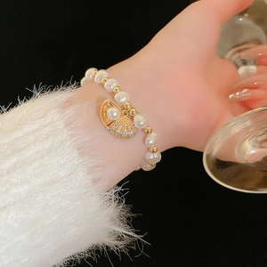 Detailed close-up of a pearl bracelet with a golden shell charm and zircon inlay
