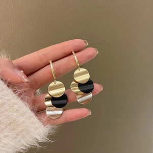 Close-up of vintage geometric gold and black discs drop earrings held in hand