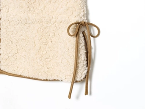 Detail of adjustable brown drawstring on a beige lamb wool vest with soft texture