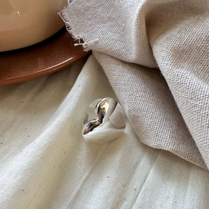 Detailed view of an adjustable silver heart ring on a minimalist linen fabric background