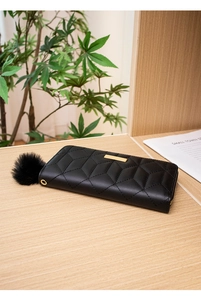 Close-up of black quilted long wallet with golden metal bar and furry pom-pom charm