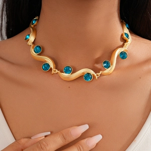 Close-up of a gold wavy necklace with inlaid blue round crystals on model neck
