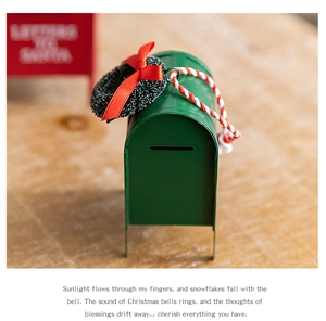 Macro detail of a green metal Santa mailbox ornament with wreath and woven lanyard