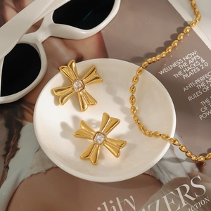 Detailed view of gold cross earrings with zircon gemstone on white ceramic dish