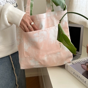 Dettaglio della borsa tote in tela tie-dye rosa con tasca frontale e manici verdi