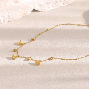 Detail of 18K gold butterfly necklace with zircon stones on textured beige surface