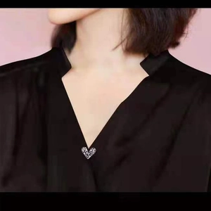 Close-up of sparkling silver heart brooch with zircons on black V-neck collar detail