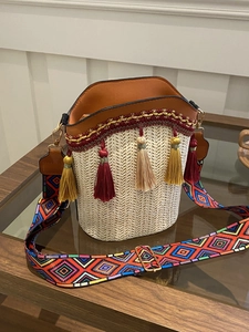 Detail of woven straw bucket bag with colorful geometric strap and red bohemian tassels