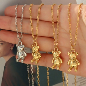 Detailed view of four bear-shaped necklaces in gold and silver finish held by hand