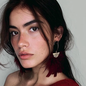Close-up of vintage gold geometric earrings with elegant dark red feather tassels