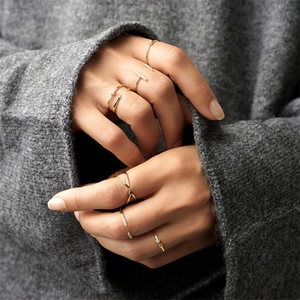 Detail of minimalist gold layered rings with clear gemstones worn with grey knitwear