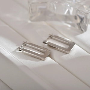 Polished silver stainless steel rectangular hoop earrings on a textured display base