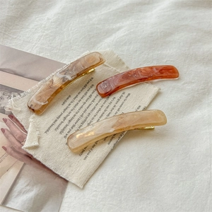 Elegant marble pattern hair clips in amber and beige tones on neutral fabric background