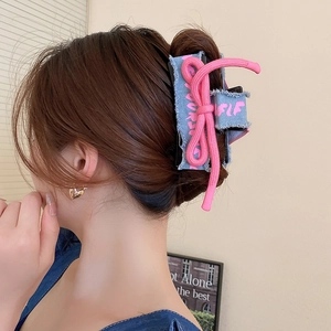 Detail of blue denim hair claw clip featuring pink woven bow and frayed edges