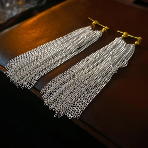 Macro shot of gold ear studs with long layered silver chain tassels on dark leather