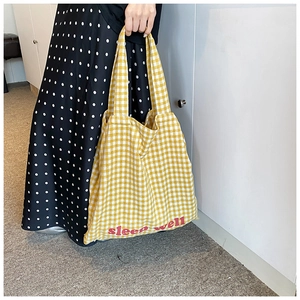 Detail of yellow checkered tote bag featuring pink sleep well text and fabric texture