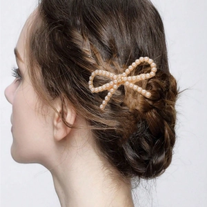 Elegant gold bow hair clip with pearls and rhinestones shown on braided hair