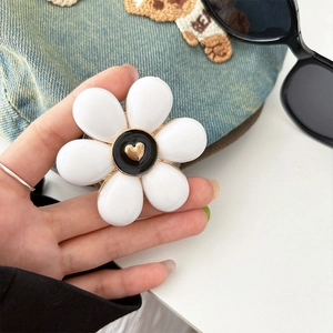 Close-up of white flower phone grip with black center and golden heart on denim background