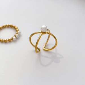 Close-up of golden cross-over open ring featuring a white freshwater pearl accent