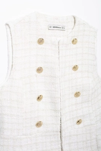 Detail view of white tweed vest with golden double-breasted buttons and BBWMWOMAN brand label