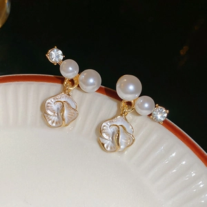 Boucles d'oreilles fleurs dorées avec nacre et perles blanches sur un plateau