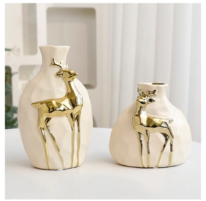 Detail of modern cream ceramic vases with embossed golden deer design on tabletop