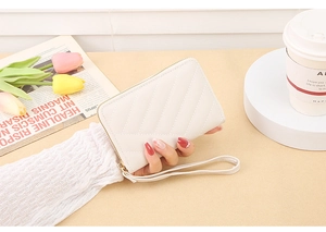 Detailed close-up of white quilted zip wallet with wrist strap held against lifestyle decor